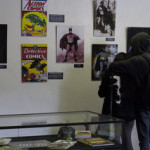 A couple looks at a wall display depicting some of the various actors who have portrayed Superman or Batman on film.